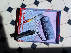 A paint tray that has been used. It has a paint brush and a roller in it