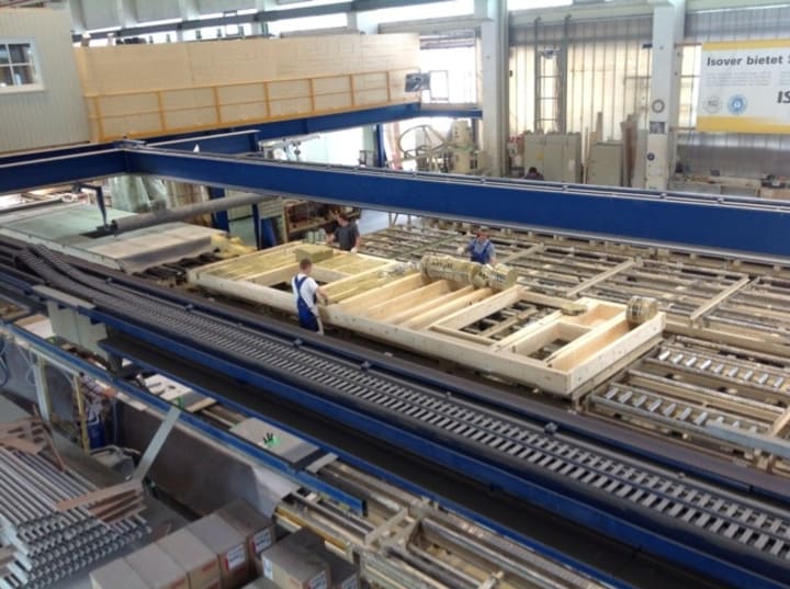 Walls lying on a conveyor belt as men work on them.