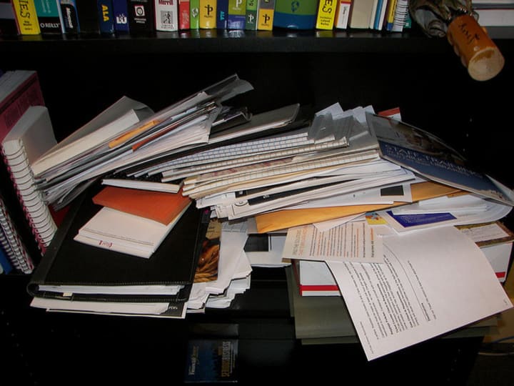 a very messy desk with piles of overflowing paper.