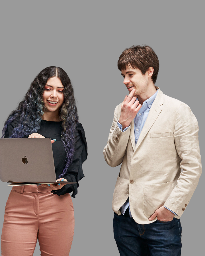 Smiling woman explains code on laptop screen while man standing beside her looks on with curiosity