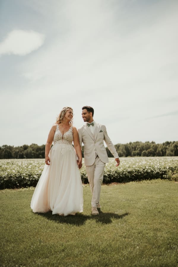Authentischer Moment: Braut und Bräutigam laufen glücklich lachend Hand in Hand über eine Wiese vor einem blühenden Feld im Garten des Hotel Hennies Isernhagen.