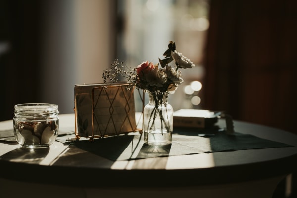 Elegante Hochzeitsdekoration im Detail: Eine kleine Glasvase mit Blumen und ein Dekoglas auf einem Tisch im stimmungsvollen, warmen Gegenlicht im Hotel Hennies Isernhagen.