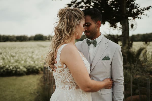 Inniges Hochzeitsfoto vom Brautpaar bei einer Umarmung auf der Wiese am Hotel Hennies in Isernhagen, Hannover. Die Braut im floralen Spitzenkleid und der Bräutigam im hellgrauen Anzug stehen Stirn an Stirn vor einem weiten Feld mit weißen Blüten.