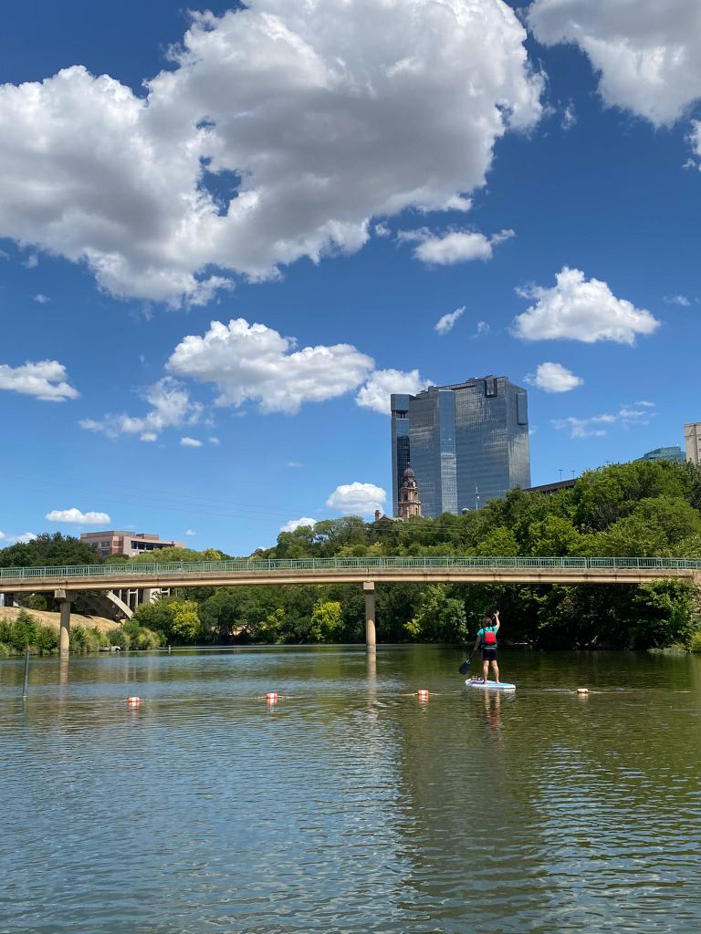 Moving along the Trinty River in a Paddleboard with Fort Worth downtown in the background on a beautiful day