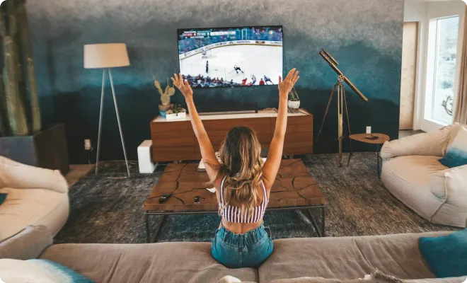 Woman cheering on her favorite hockey team on a large flat screen TV in her living room