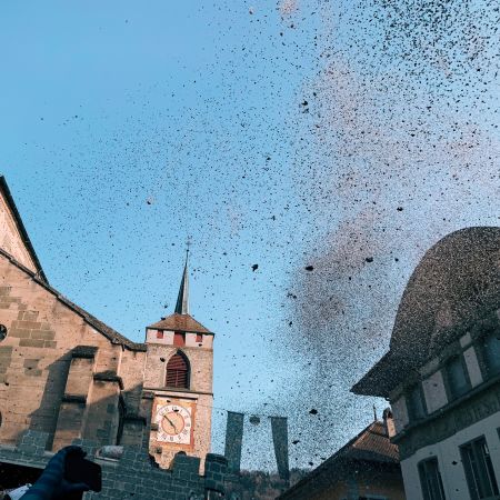 Un nuage de confettis tombe sur la place de marché. Au second plan, l'Eglise St-Etienne.