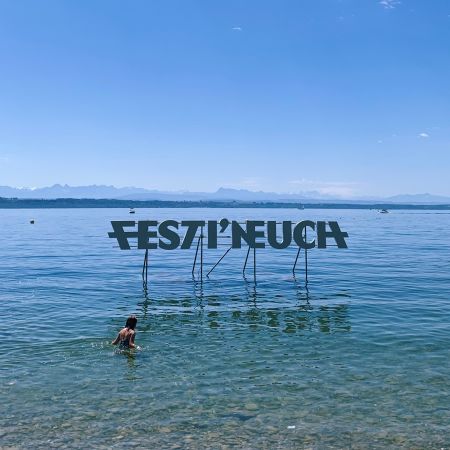 Festi'Neuch écrit en grande lettre sur le lac. Une personne se baigne devant le panneau.