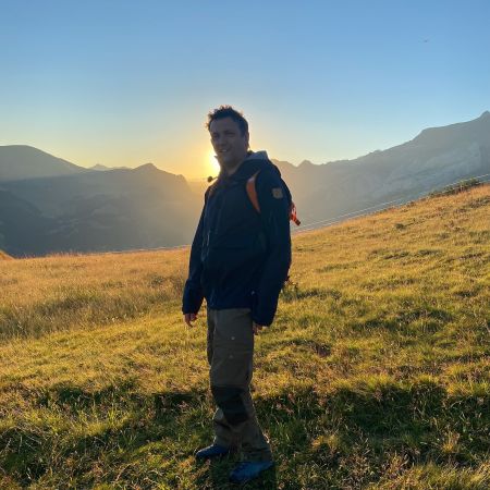 Me wearing trekking gear in the mountains. In the backround, the sun is rising.