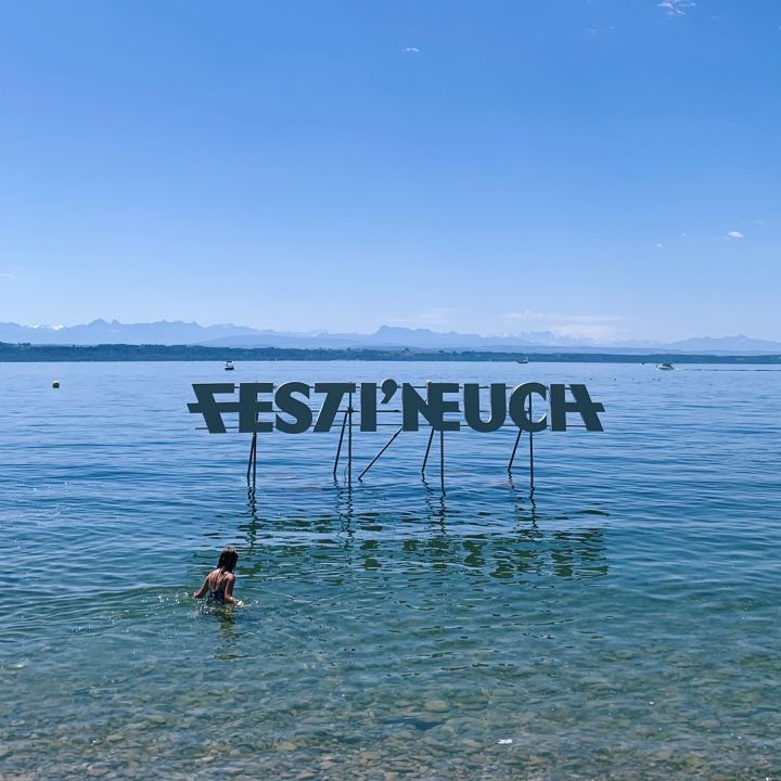 Festi'Neuch écrit en grande lettre sur le lac. Une personne se baigne devant le panneau.