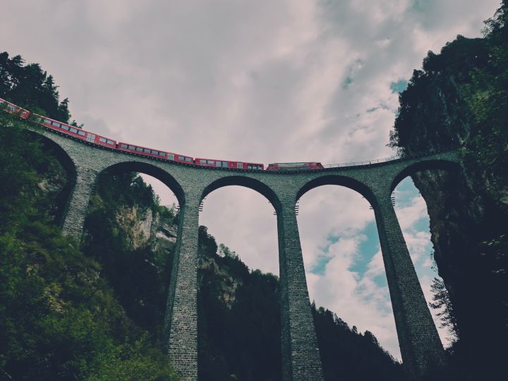 Le Viaduc de Landwasser vu depuuis le bas. Un train le traverse de gauche a droite avant d'entrer dans le tunel dans la paroi rocjeuse qui se trouve directement apres le viaduc