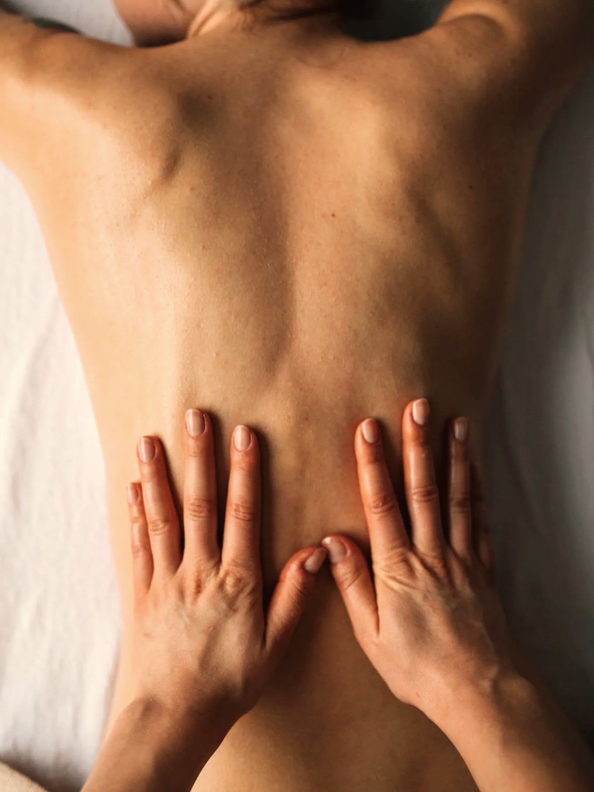 Both palms flat on a client’s back, mid-technique — hands-on body work in a Miami studio.
