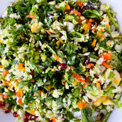 Close-up of colorful Confetti Salad with shredded vegetables and pomegranate seeds in a white bowl