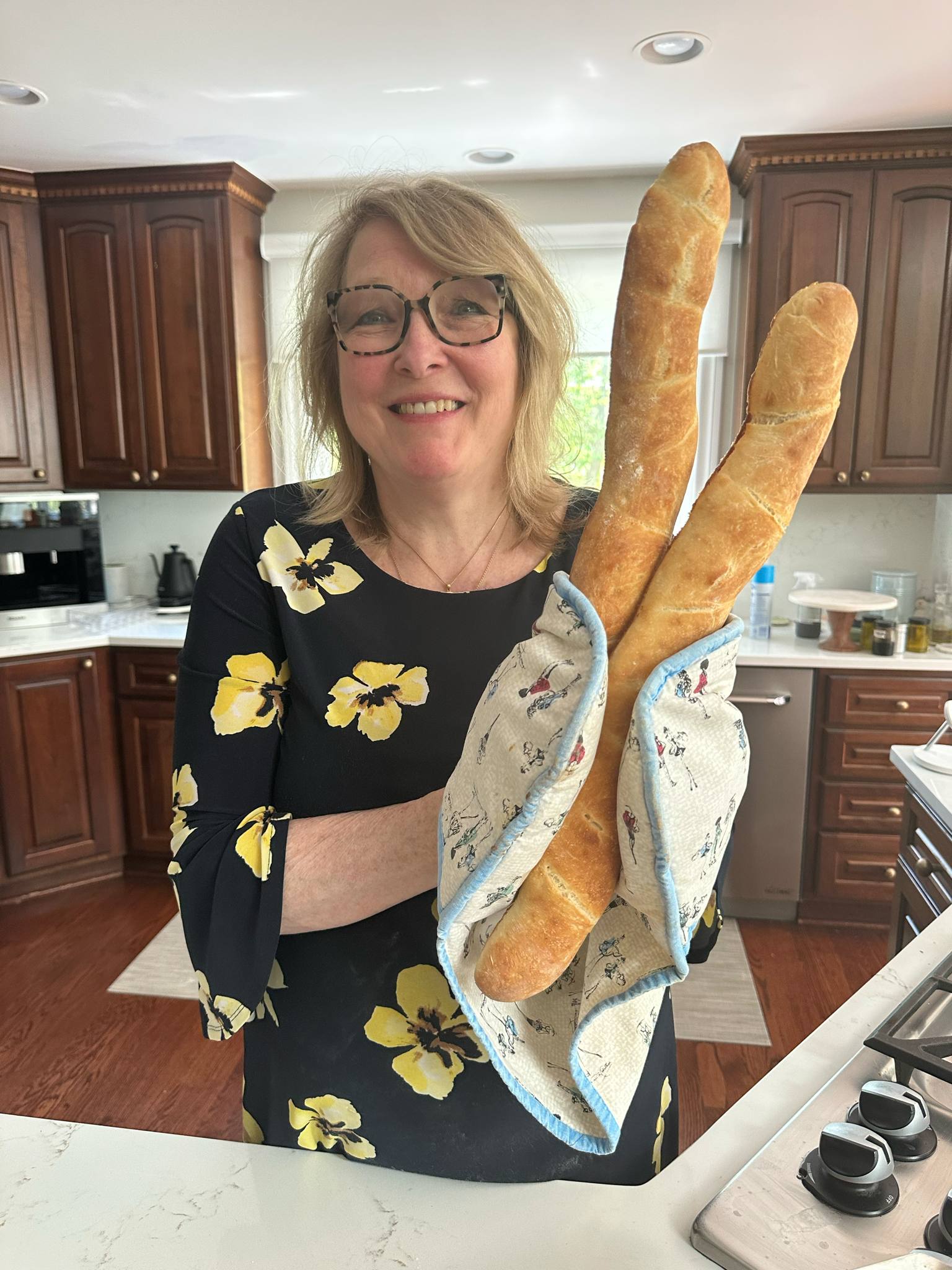 Cindy Juncaj, CEO of bon COOK, smiling and holding two freshly baked French baguettes in her kitchen
