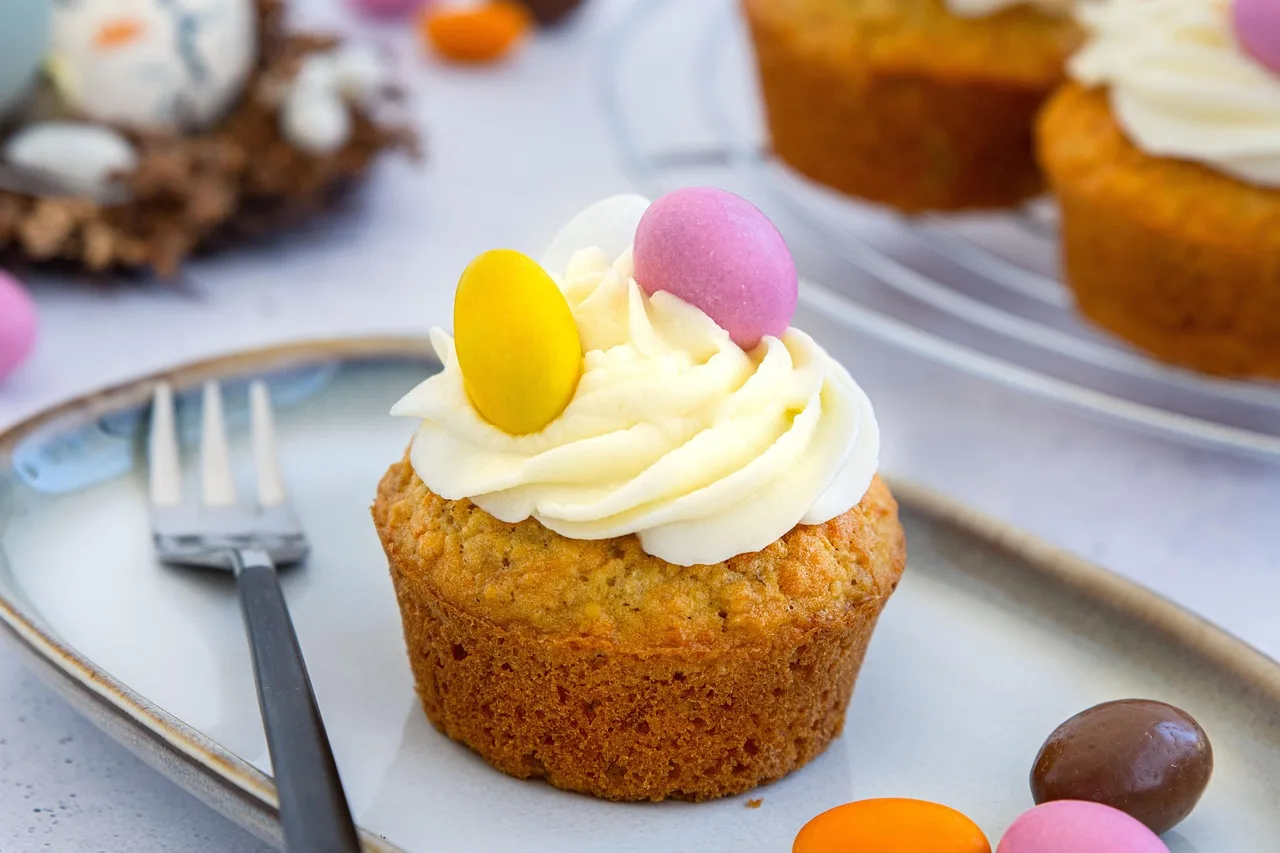 Easter-themed lemon poppyseed muffin topped with vanilla frosting and colorful candy eggs on a dessert plate