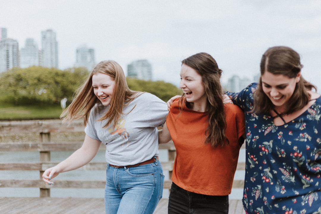 Three city women walking together with their arms draped over each other's shoulders. 