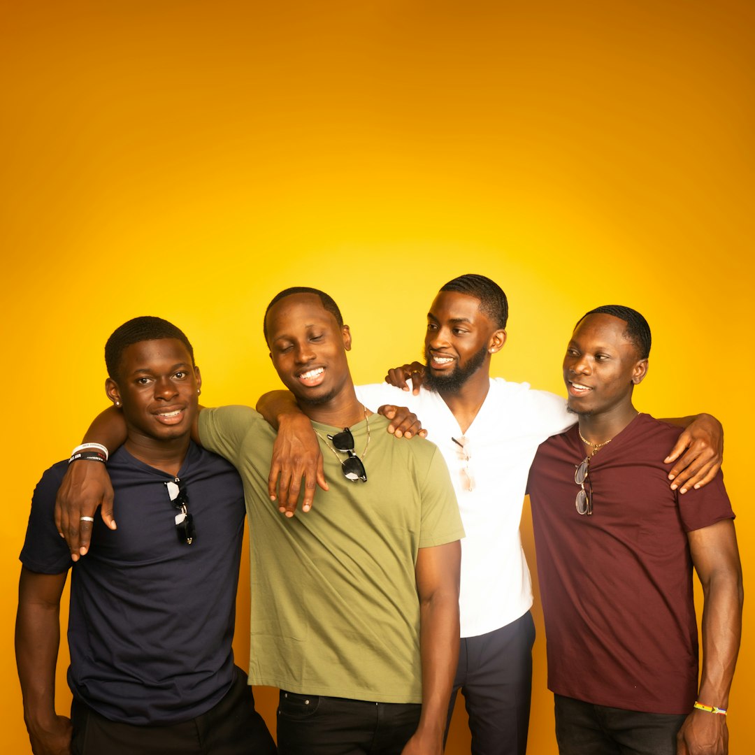 A pic of four friends (male) with their arms around each other against an orange and yellow background. 