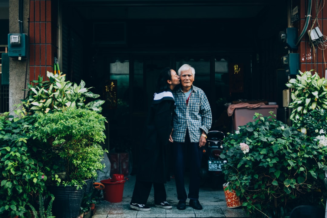 A young woman is kissing the cheek of an elderly man in front of dark store.