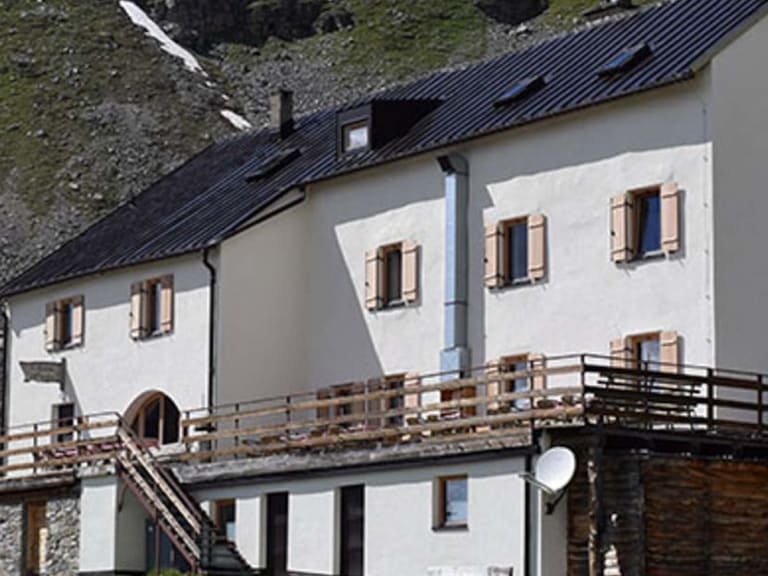 Außenansicht der Düsseldorfer Hütte mit weißer Fassade, Holzterrasse und Schweizer Flagge im Hochgebirgstal.