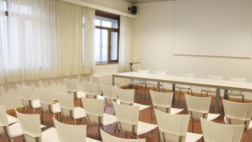 Seminarraum im Ostello La Finestra mit 40 weißen Stühlen und Whiteboard für Präsentationen.