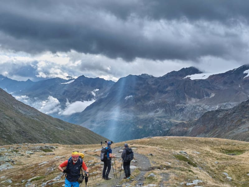 Drei Bergwanderer auf schmalem Steinpfad in der Ortler Gruppe, im Hintergrund Gletscher und felsiges Bergpanorama