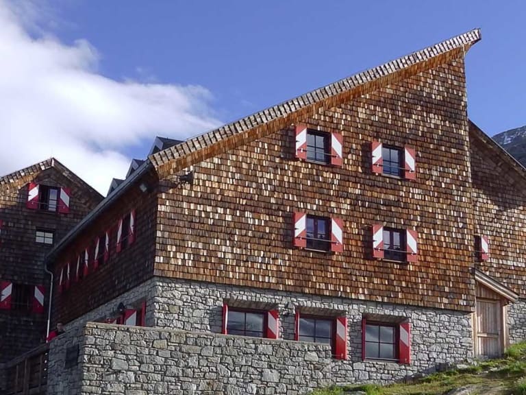 Die Kürsinger Hütte zeigt ihre traditionelle Holzschindelfassade vor der imposanten Bergkulisse der Hohen Tauern.