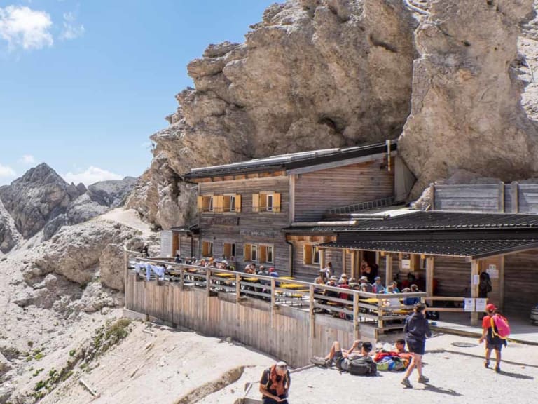 Zahlreiche Bergwanderer auf der großen Sonnenterrasse der Grasleitenpasshütte vor Dolomiten-Panorama.