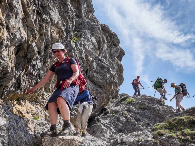 Vier Bergwanderer steigen an einem Stahlsicherungsseil einen gesicherten Kalkfelsweg in Liechtenstein ab.