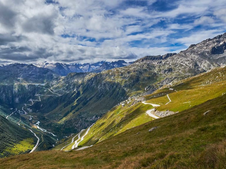 Bergwanderung über einem Walliser Alpental mit Passstraße, mäandrierendem Fluss und vergletscherten Gipfeln.