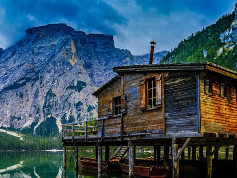 Holzgebäude am türkisfarbenen Pragser Wildsee in den Dolomiten nahe dem Gasthof Brückele Ausserprags mit Bergspiegelung.