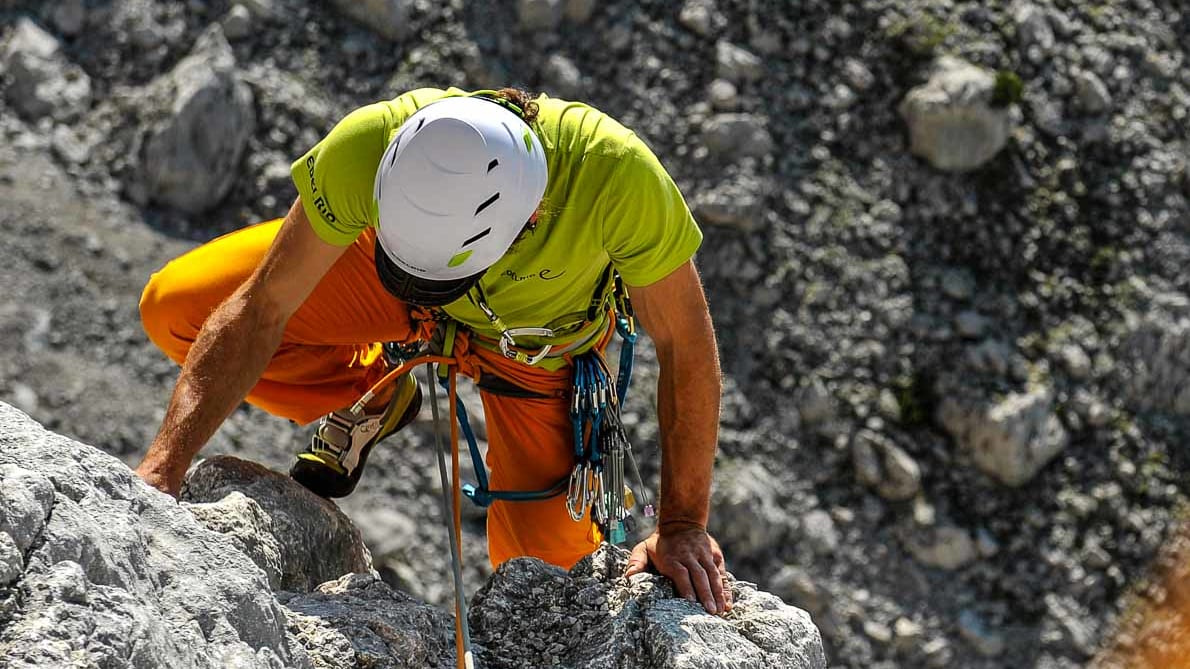 Kletterer mit weißem Helm und Klettergurt übersteigt eine Felskante aus Kalkstein im Tannheimer Tal bei Sonnenlicht