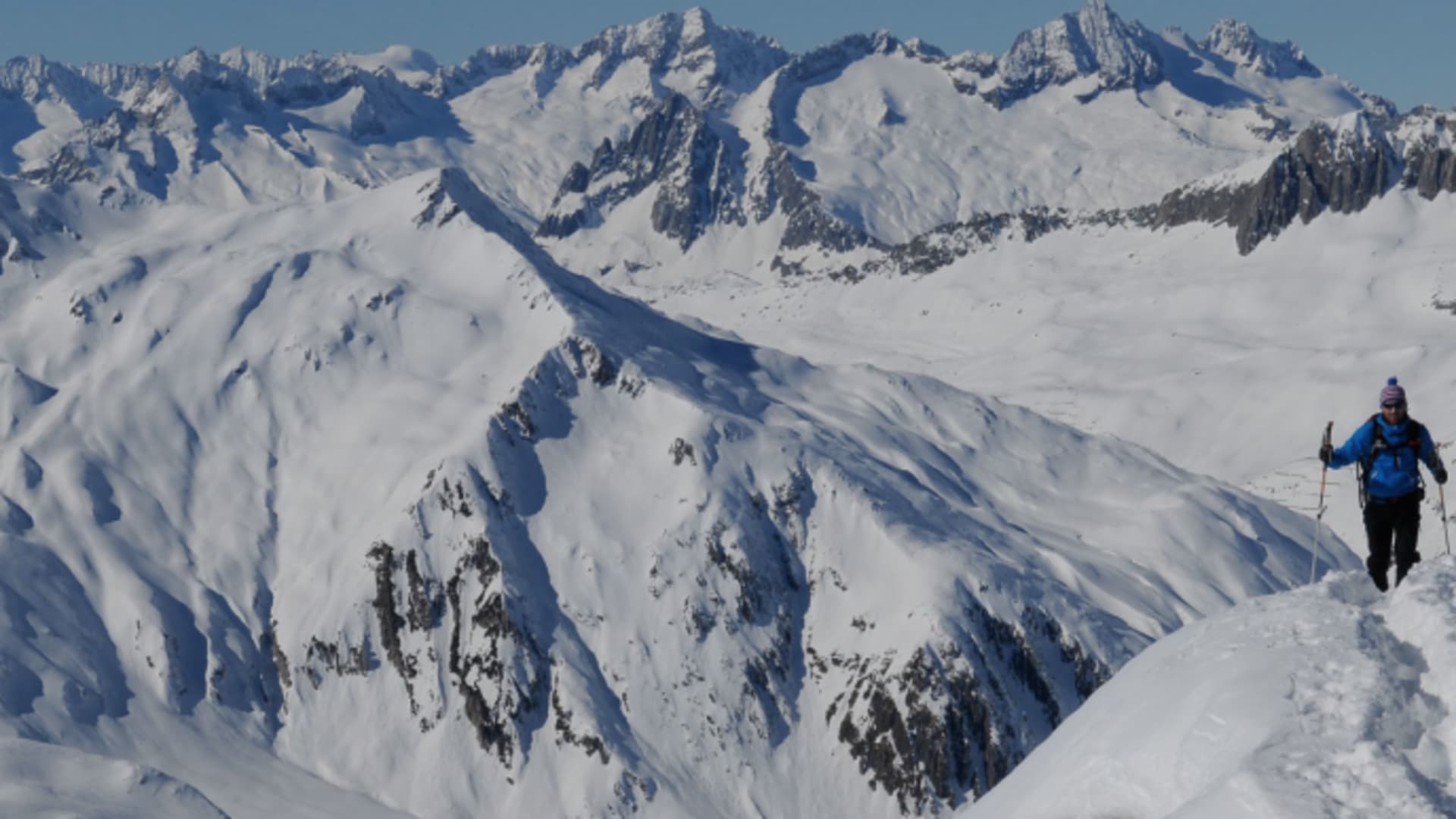 Skitourengeher mit Skistöcken auf verschneitem Grat bei Disentis im Winterpanorama.
