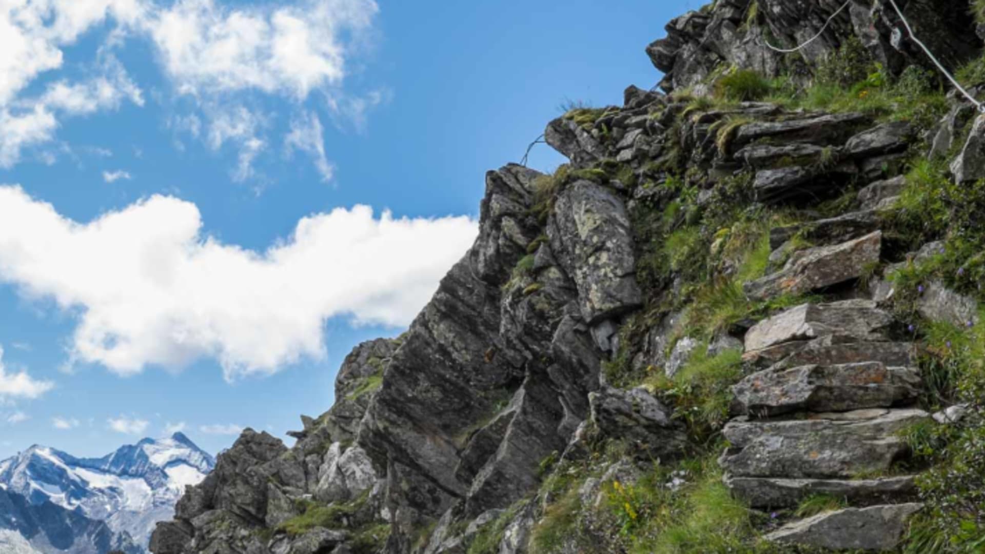 Bergwanderung auf der Dreiländertour im Zillertal: felsiger Berggrat mit Drahtseil und weitem Gipfelpanorama mit Schnee