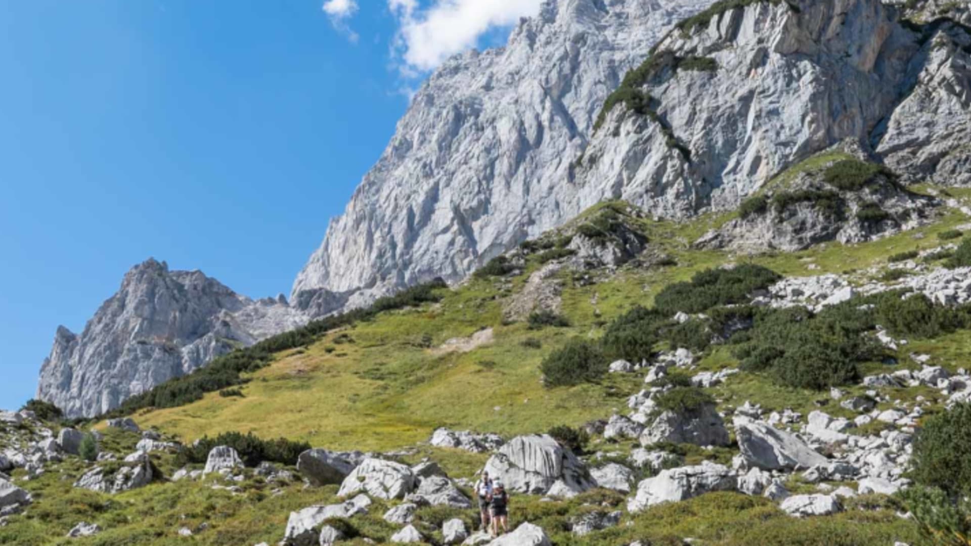 Bergwanderergruppe mit Rucksäcken steigt am Dachstein einen felsigen Hangweg entlang einer Kalksteinwand auf.