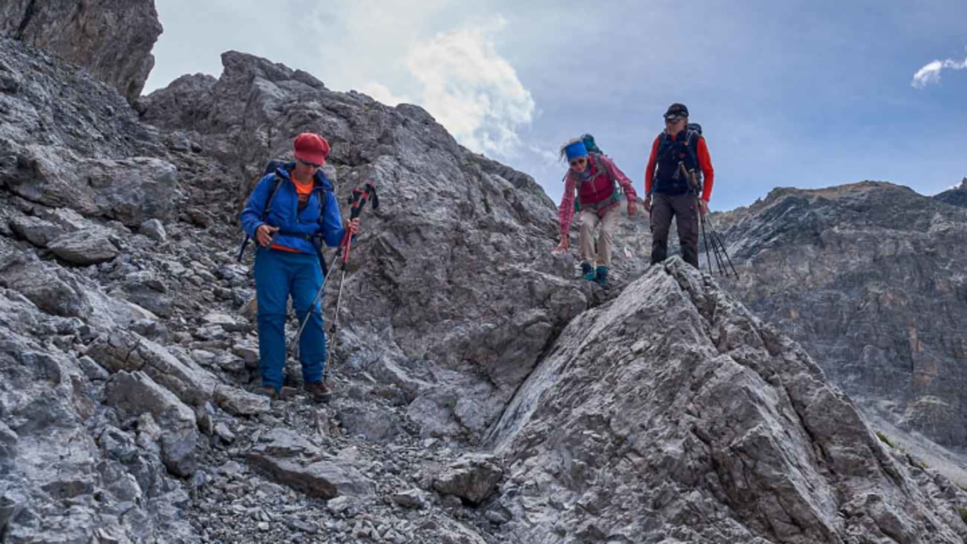 Drei Bergwanderer steigen auf einem felsigen Grat im Engadin ab, mit rot-weißer Wegmarkierung.