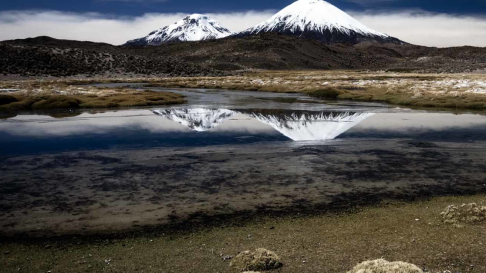 Expedition in den bolivianischen Anden: Zwei schneebedeckte Vulkankegel des Parinacota spiegeln sich in einer Hochlandlagune.