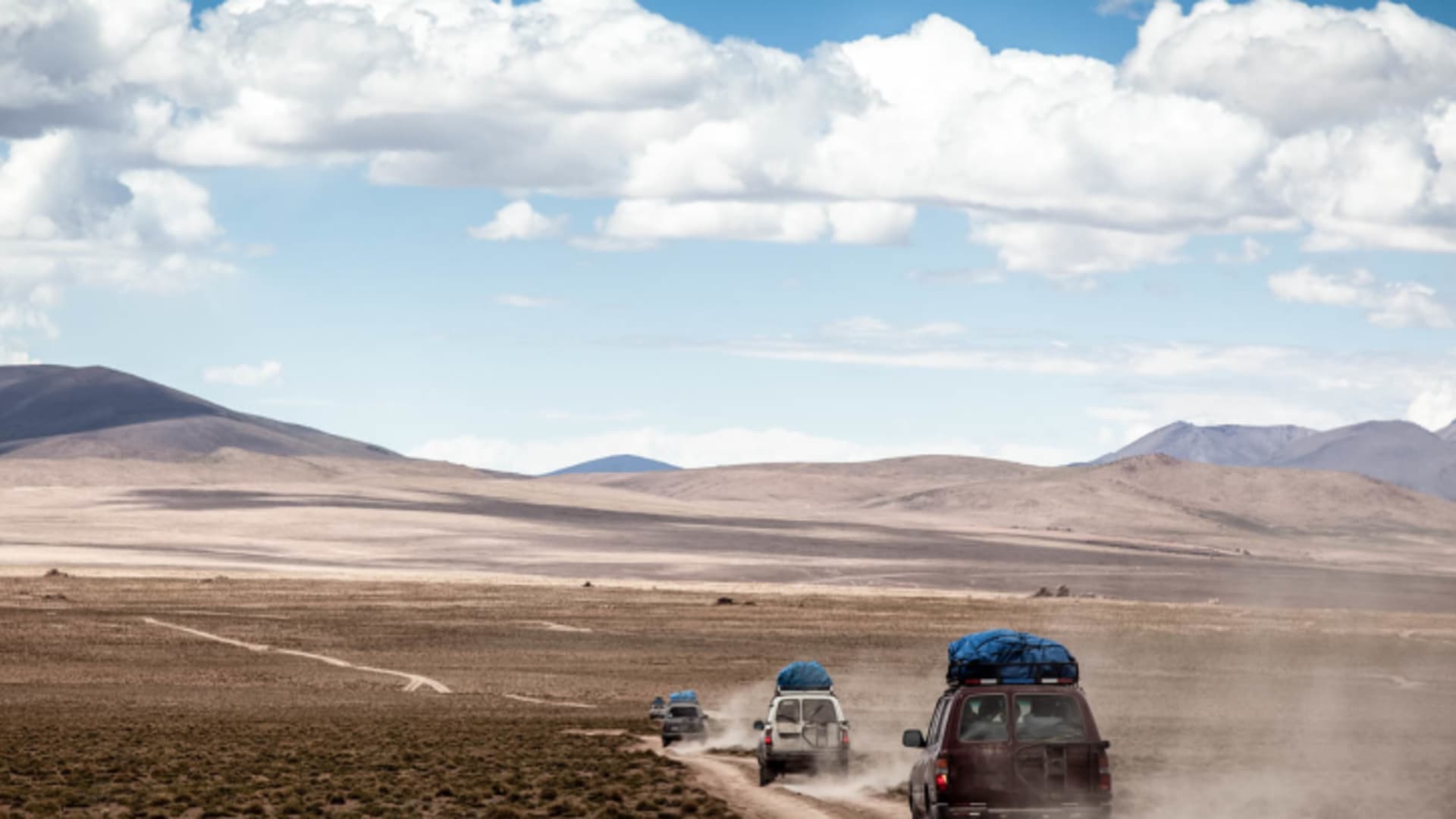 Expedition in Bolivien: Drei Geländefahrzeuge mit blauem Dachgepäck fahren auf einem Schotterweg