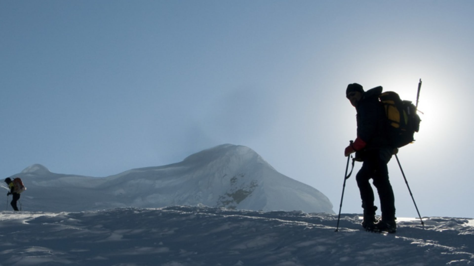 Vier Höhenbergsteiger mit Steigeisen und Stöcken im Gegenlicht auf dem verschneiten Gletscherplateau des Mera Peak.