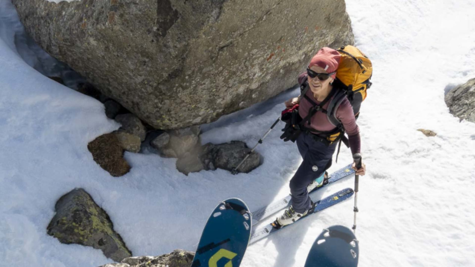 Skitourengeher mit Fellen steigt in den Albula-Alpen neben einem grossen Felsblock auf einem schneebedeckten Hang
