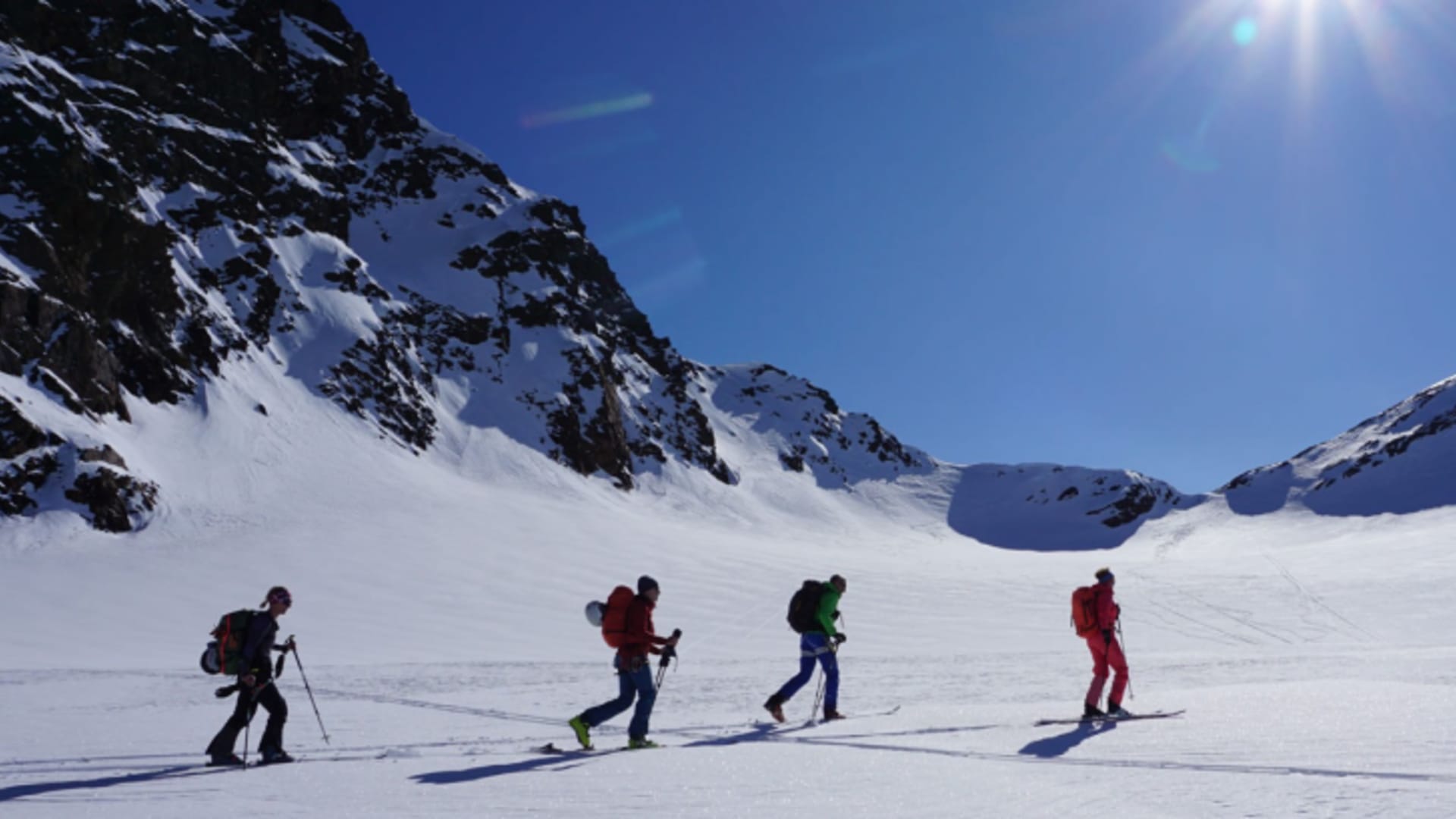 Vier Skitourengeher traversieren ein sonniges Schneeplateau im Ortlergebiet mit Sonnenstern.