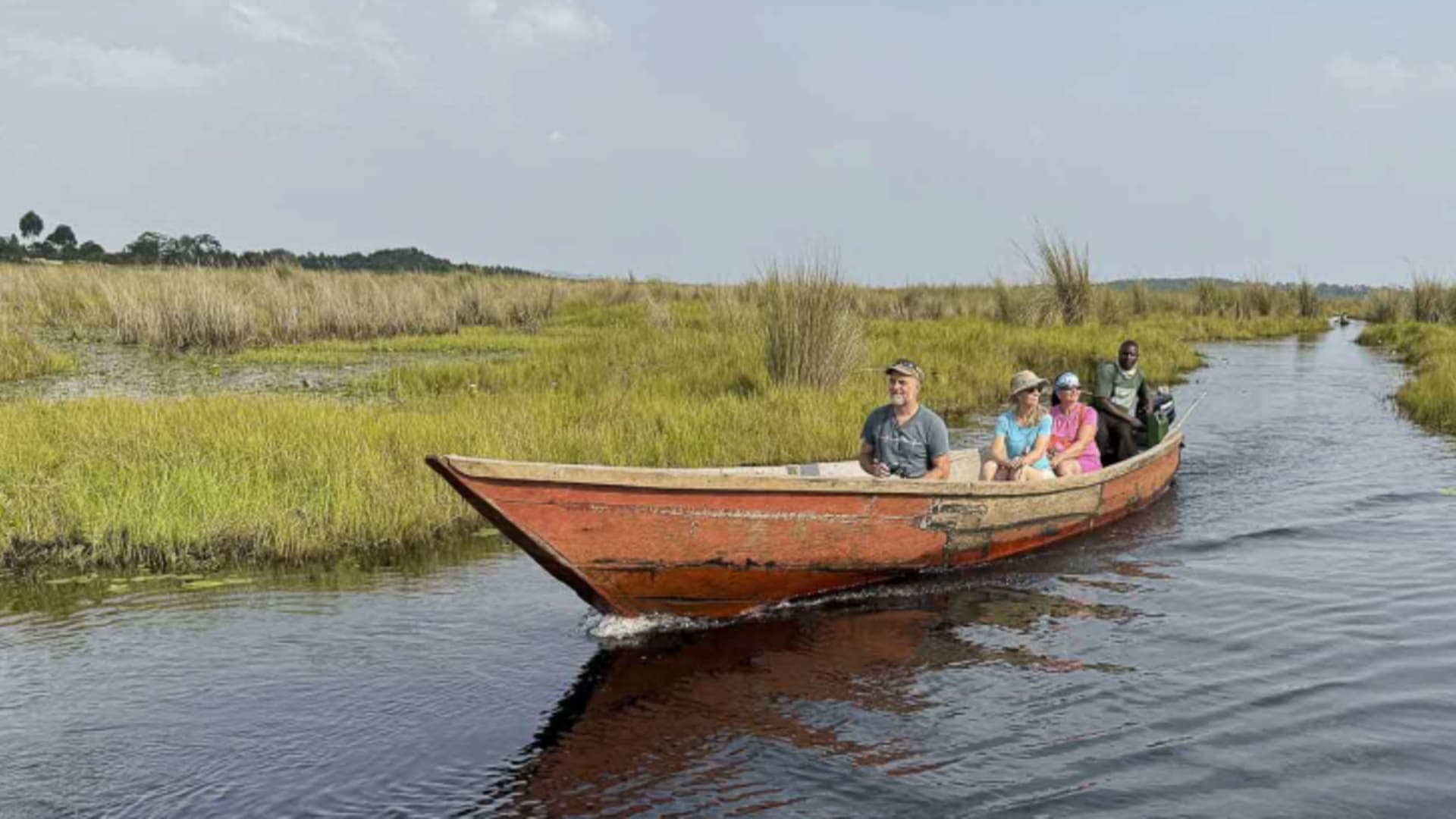 Trekking in Uganda: Vier Personen im roten Holzboot auf einem Sumpfkanal bei Entebbe mit Schuhschnabel-Beobachtung.