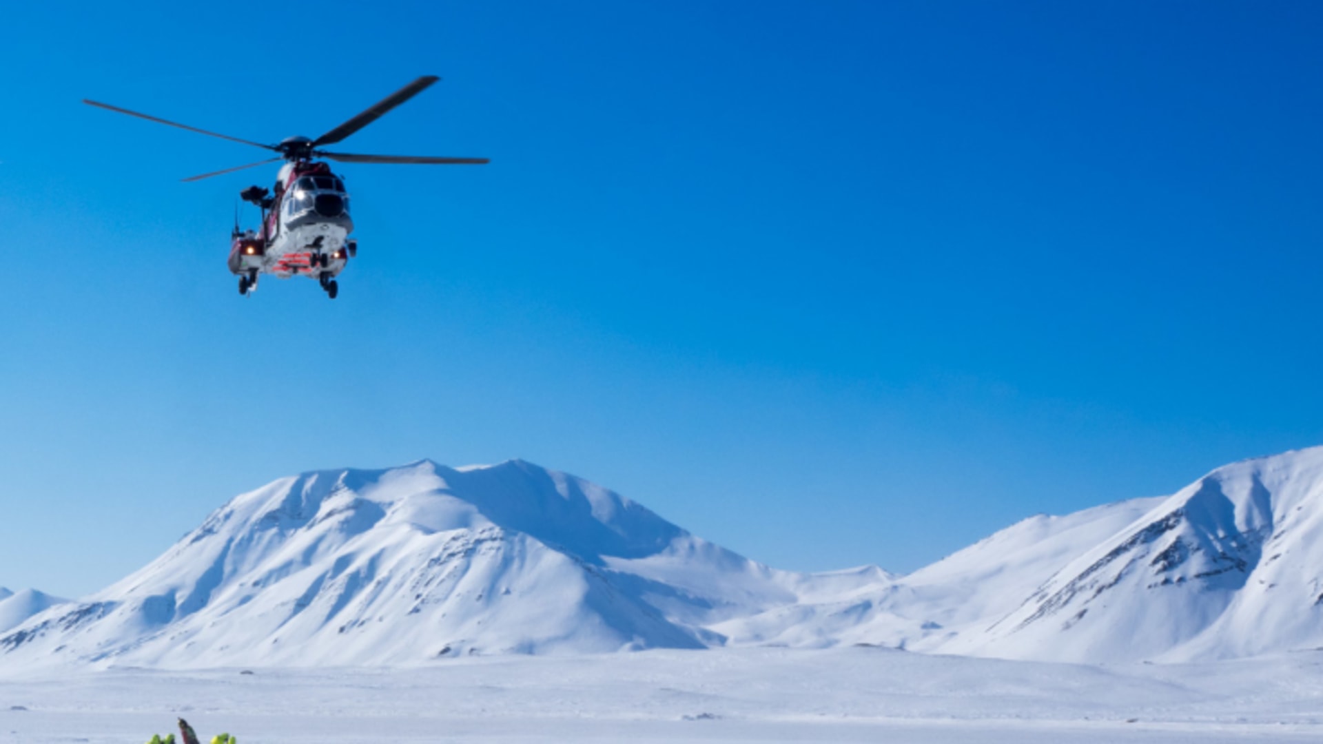 Rescue mit Helicopter auf verschneiter Ebene: Personen in gelb-grünen Overalls neben Ausrüstungspaketen
