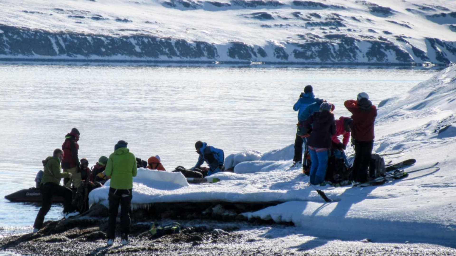 Bergsteigergruppe steigt auf Spitzbergen aus einem Schlauchboot an schneebedecktem Fjordufer aus, Winterbedingungen.