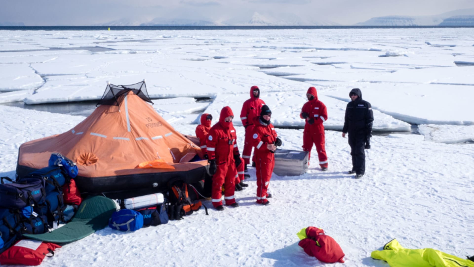 Bergtour Polarcode Training auf Meereis in Spitzbergen: fünf Bergsteiger in Überlebensanzügen neben Rettungsfloß.