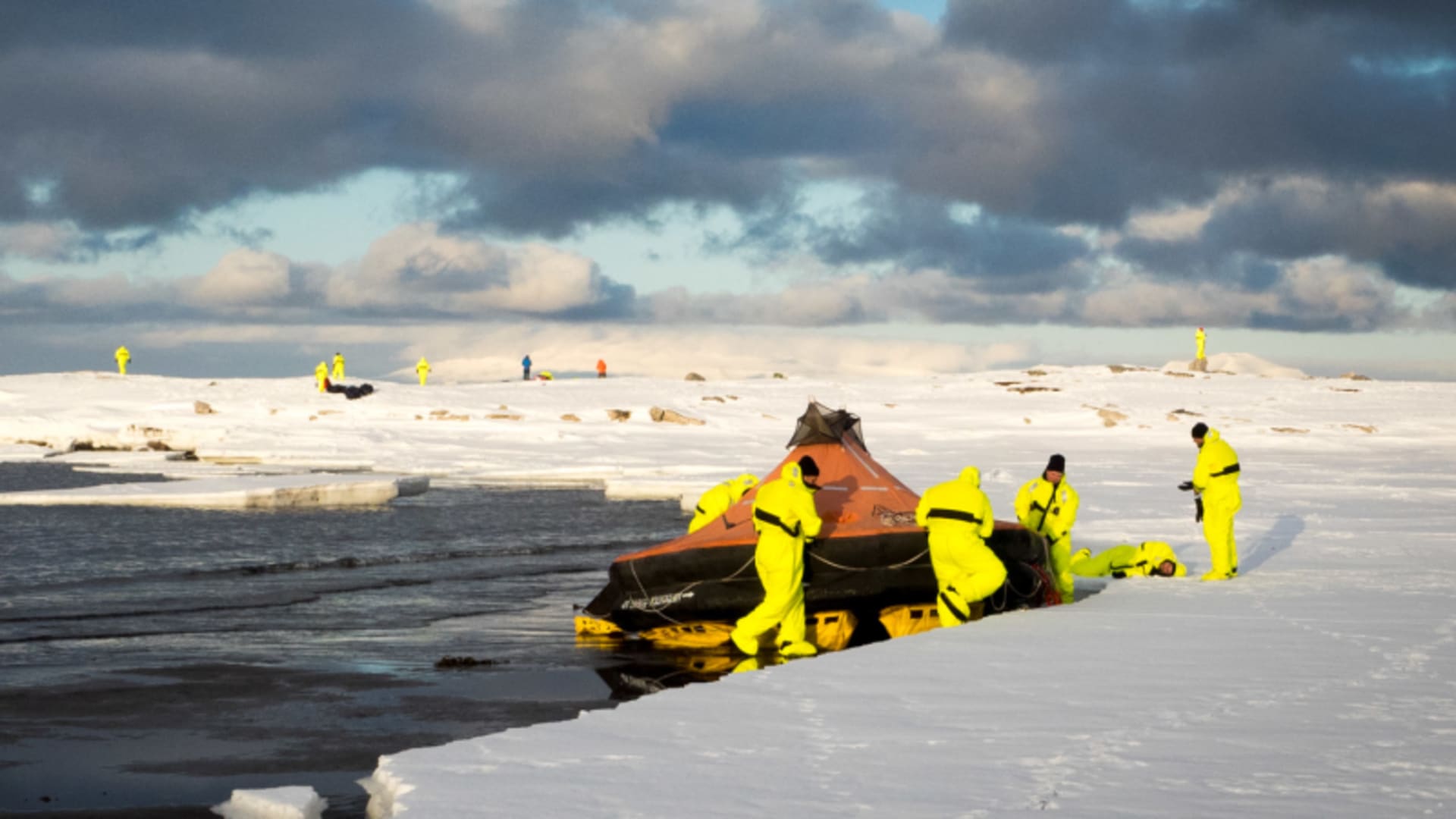 Bergtour Polarcode Training Spitzbergen: Bergsteigergruppe in gelben Überlebensanzügen schiebt Rettungsfloß am Eisrand ins Wasser.