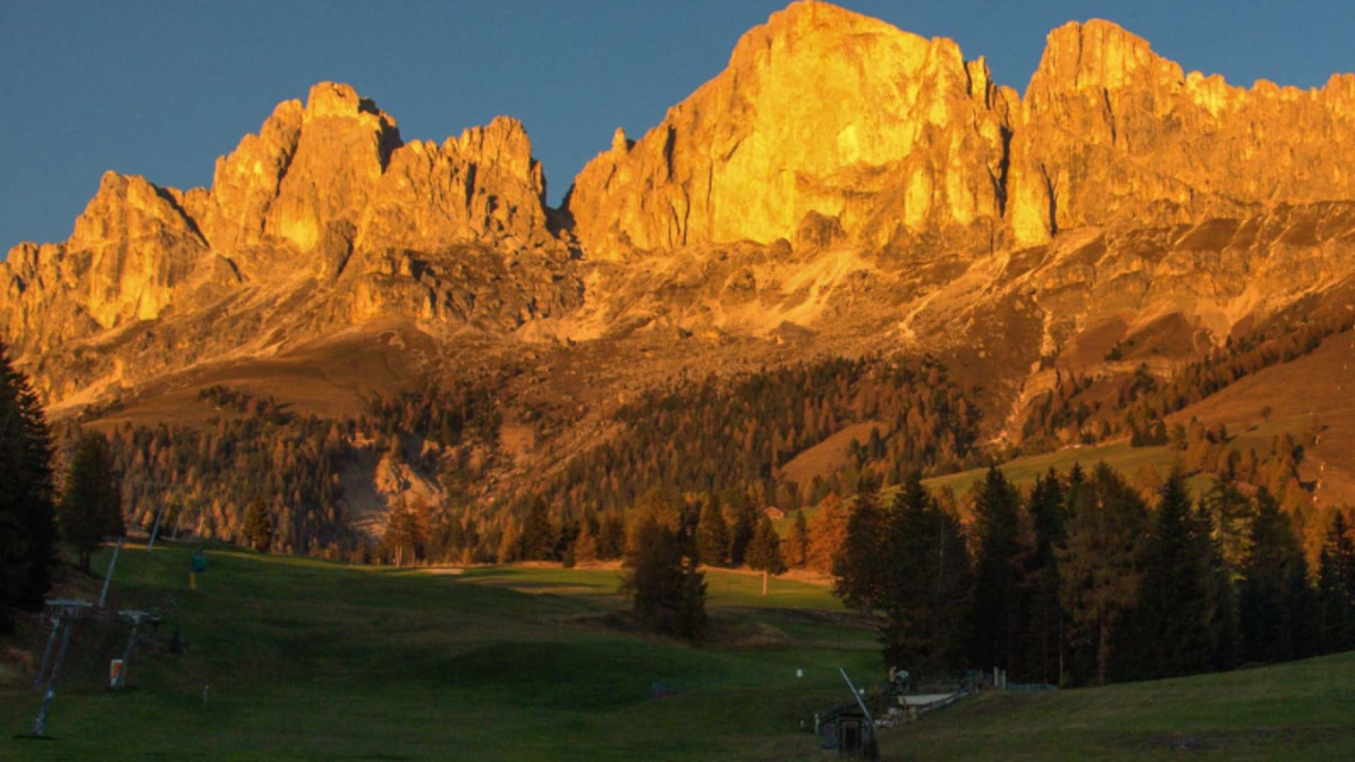 Bergwanderung in den Dolomiten: Felsmassiv mit senkrechten Kalksteintürmen im orangeroten Alpenglühen bei Sonnenuntergang.