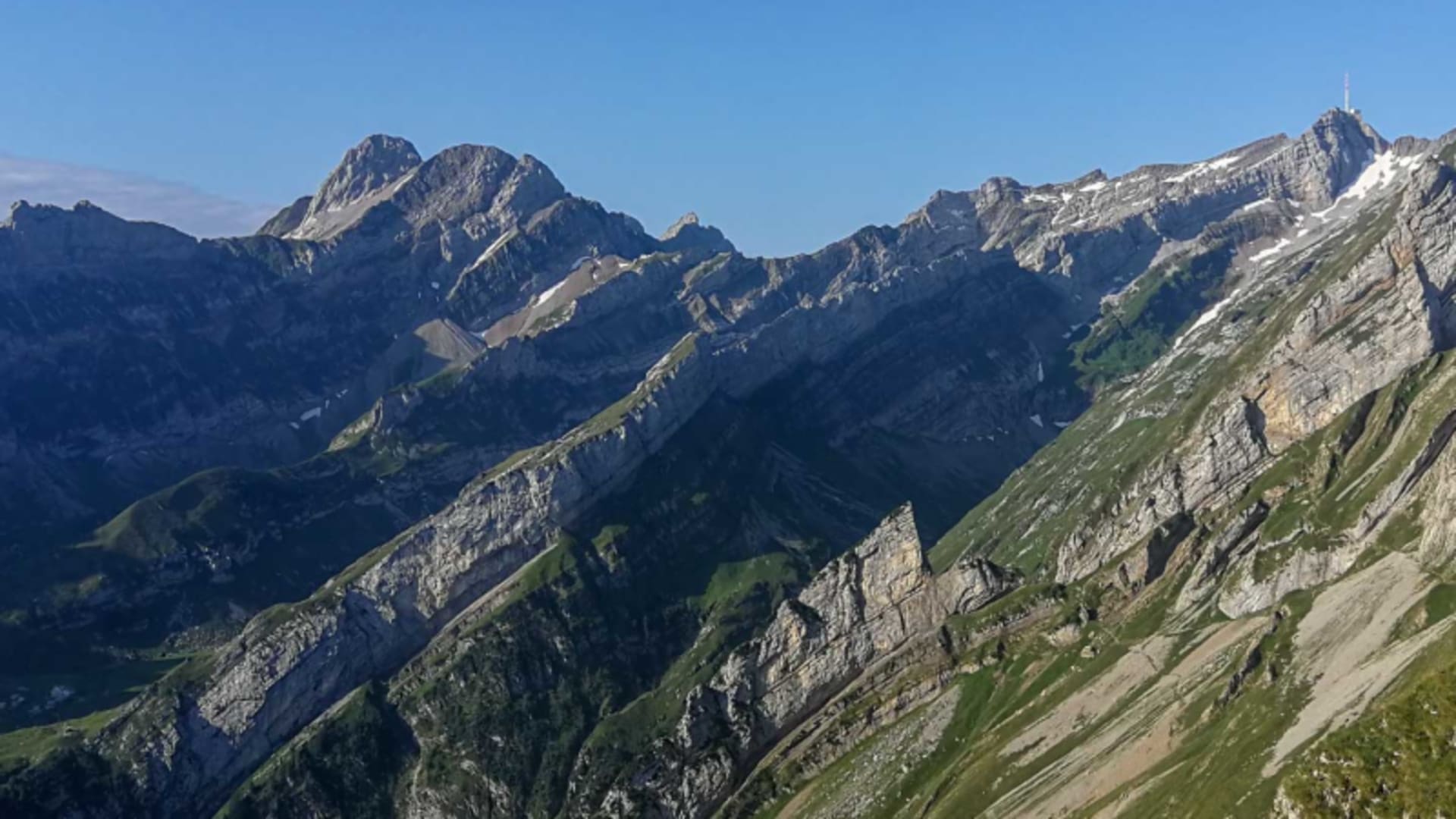 Bergwanderung am Säntis: Felsgrat der Altenalptürme mit geschichteten Kalksteinwänden, Antenne auf dem Gipfel und blauem Himmel.