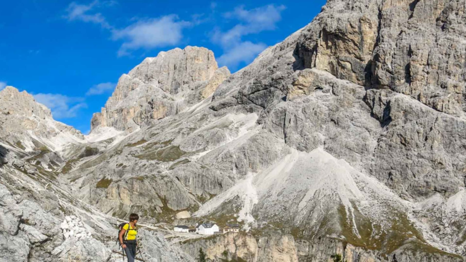 Bergwanderer auf felsigem Pfad im Kalkstein-Kammdurchgang mit Berghütte im Hintergrund, Dolomiten.