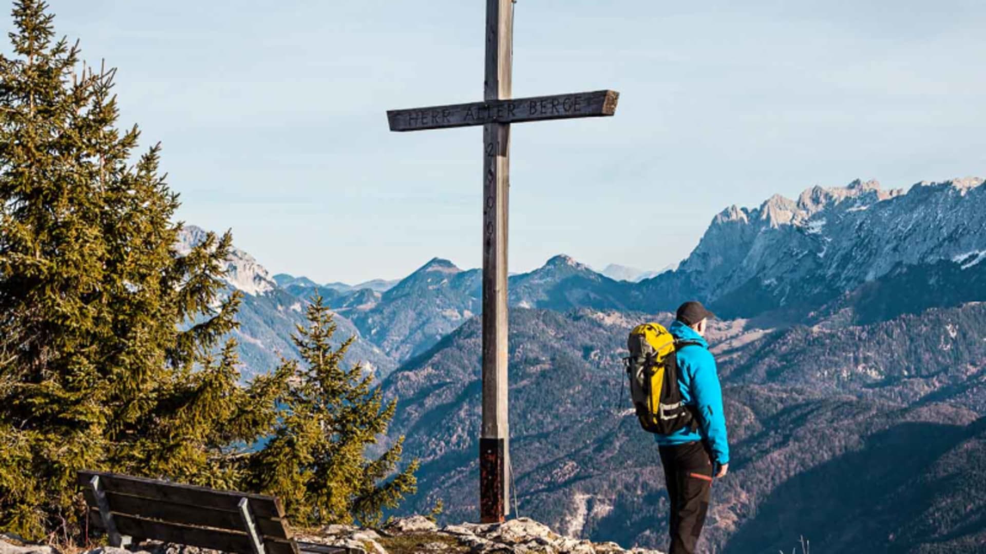 Bergwanderer steht am Gipfelkreuz mit Inschrift HERR ALLER BERGE bei der Bergwanderung im Wilden Kaiser.
