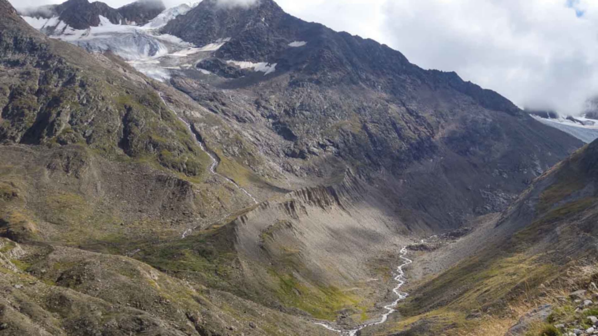 Bergwanderung in der Bernina: Schotterweg durch karges Hochtal mit mäanderndem Gletscherbach und Gletscherzungen im Hintergrund.