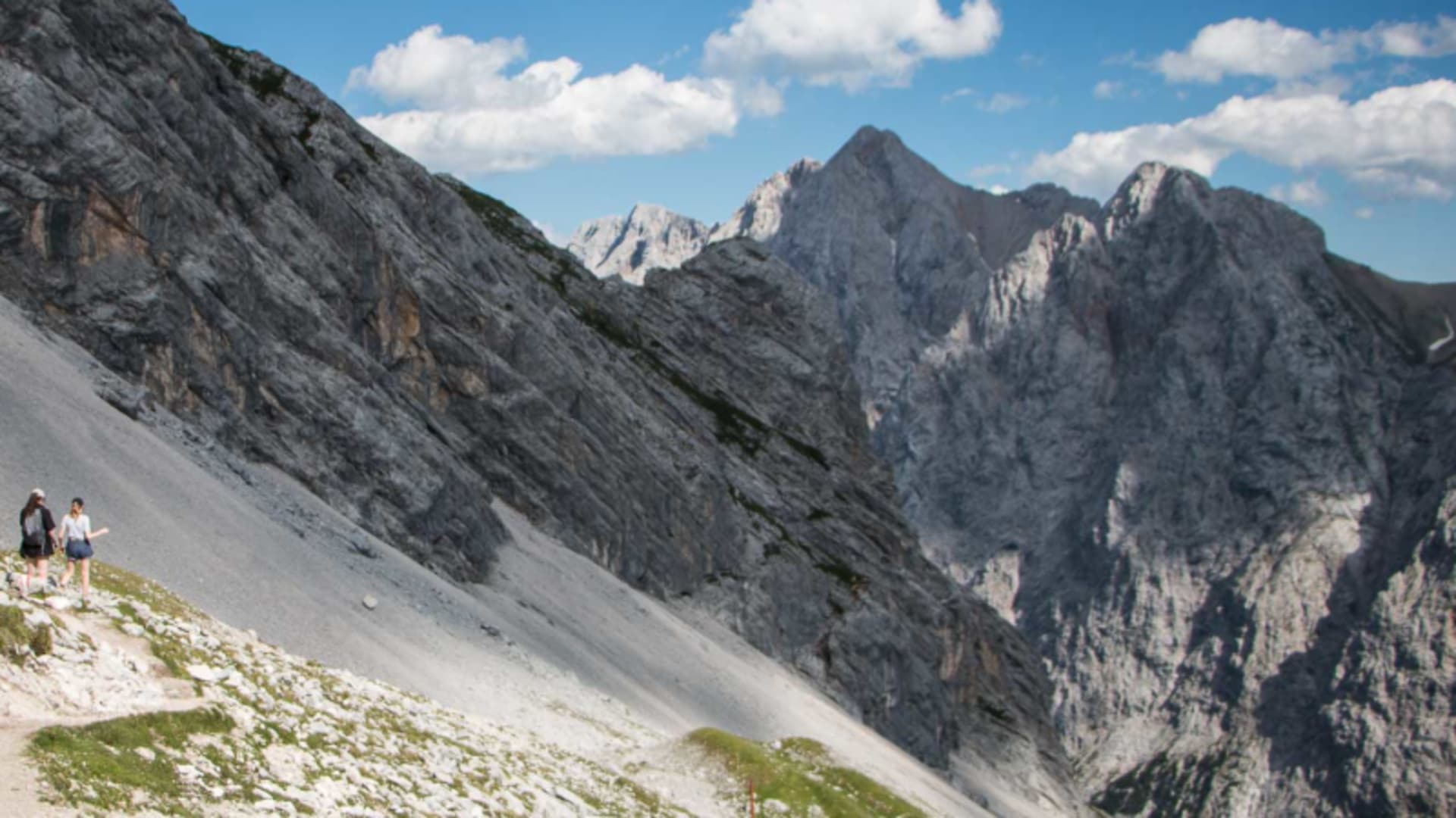 Bergwanderung an der Zugspitze: zwei Bergwanderer auf Schotterweg an steilem Kalkfelshang mit Bergpanorama.